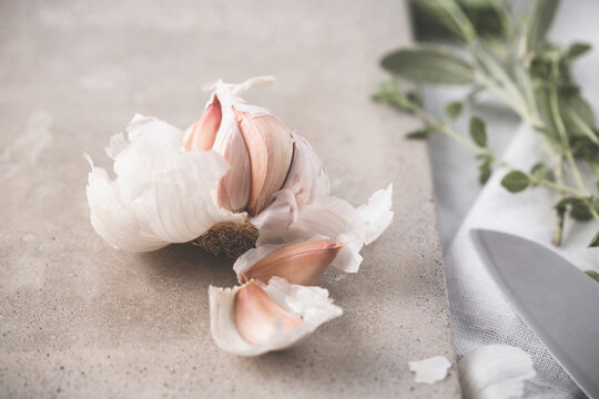 Head of Garlic Open on Cutting Board with Green Herbs and Knife Beside