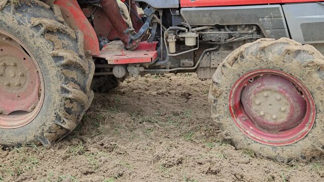 Agricultural tractor working across a rural farmland in India, plowing and preparing the soil for crop cultivation under a bright blue sky. The footage highlights modern farming practices
