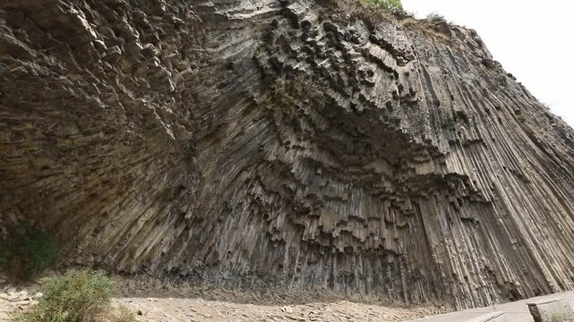 A breathtaking view of a massive cliff face composed of unique, vertical hexagonal basalt rock columns. This stunning natural geological formation looks like a giant, ancient stone organ.