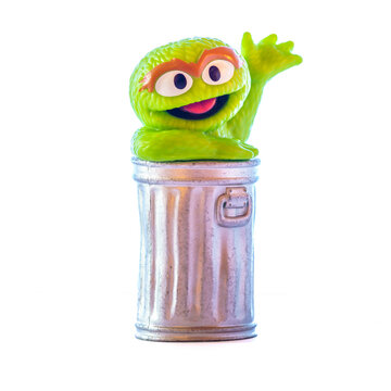 Utica, NY - Jan 6, 2026: A small Oscar the Grouch figurine from Sesame Street, shown emerging from a silver trash can with one arm raised, photographed against a plain white background