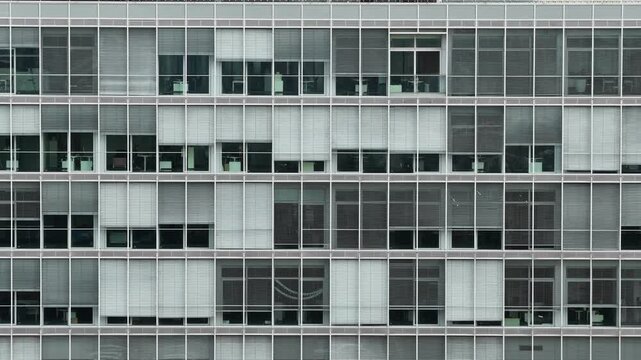 Front view of a modern office building facade with repetitive glass windows and blinds, showing corporate architecture and geometric design pattern.