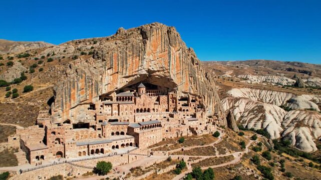 Aerial View of Selime Monastery Carved into a Cliffside in Cappadocia Turkey Under a Clear Blue Sky