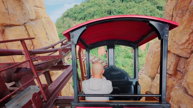 Riding on a red train through a rocky tunnel in an amusement park during a sunny day with trees in the background