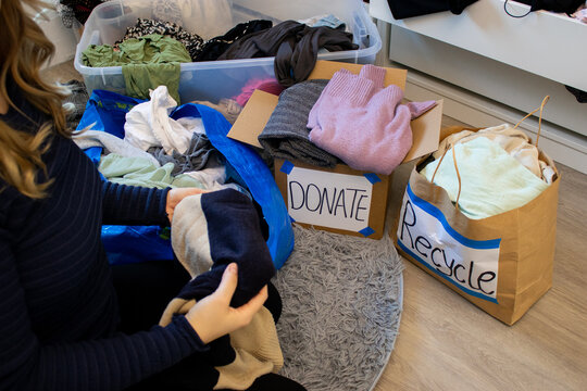 Close up of a young woman sorting clothes from her wardrobe for recycling and donation