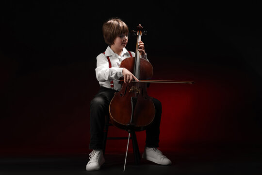Little boy playing violoncello on dark red background