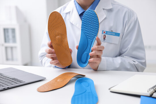 Orthopedist in medical coat with foot insoles at white desk in clinic, closeup