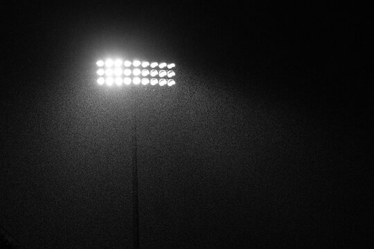 Bright illuminated stadium lights at night during a rainstorm. Great texture and mood with directional lighting. Strong, dramatic image of a sporting event