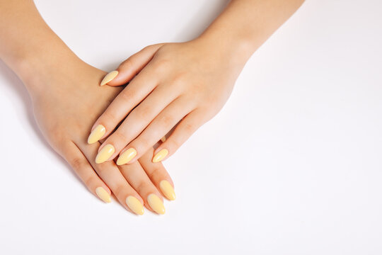 Close-up of female hands with soft pastel yellow manicure on a clean neutral background. Minimalist beauty concept, skincare and nail care aesthetic.