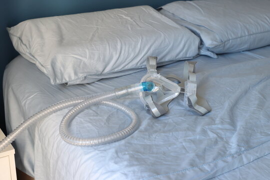 A close-up view of a CPAP mask and its corrugated tube lying on a blue-sheeted bed, suggesting sleep therapy or medical care at home