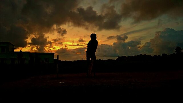 Silhouette of a cricket player playing a shot during dramatic sunset in India. Slow motion sports scene with golden sky, outdoor field, and action moment, ideal for cricket, sports themes.