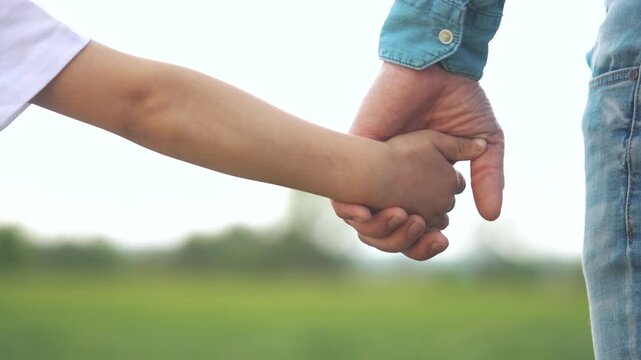 Man and a child holding hands. Close up of a father and son together. Close up of a father and son close up together. A boy and an adult grasping each lifestyle other's hands.