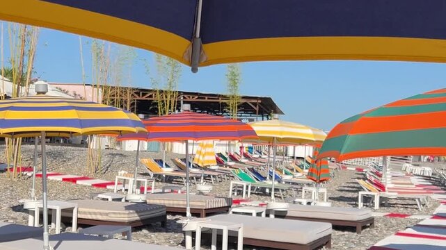 Horizontal travel video. Camera is turn. Yellow and blue umbrella, parasol close up. View of colorful deck chair, chaise longue, sun lounger on Black sea coast on pebble beach of Batumi. Relax, rest