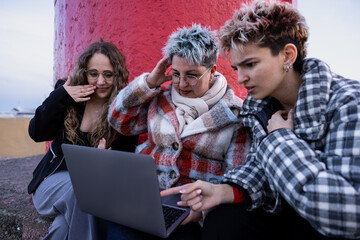 Fototapeta premium Three women looking worried while using a laptop outdoors. Concept of stress, concern and unexpected problem in a modern digital urban environment.