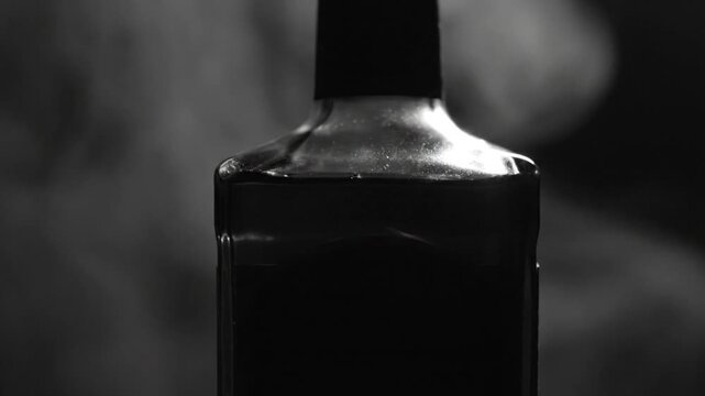 Black and white close up of liquor bottle with dark contents and smoke surrounding its form