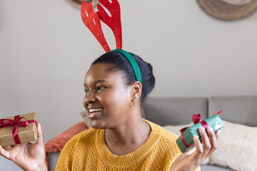 African American woman sitting on couch wearing mustard knit holding two wrapped gifts looking left