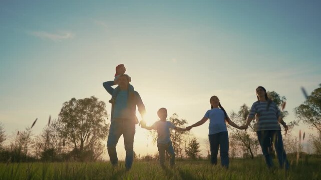 Family walking in a field. Family walking lifestyle in the park at sunset. Family walking together in summer. A family strolling through a field.