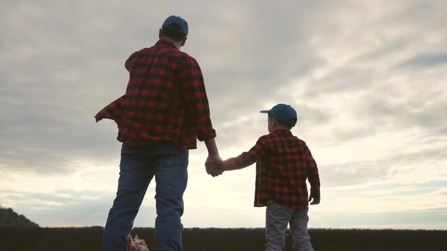 Father and son in a field. Silhouette of farmers and their son plowing a field. Family holding their father sons hand. A dad and lifestyle his son in a meadow.