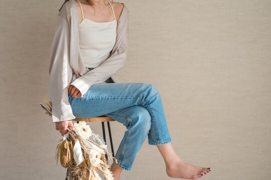 A stylish denim-clad female model sits on a chair, holding a swag or bouquet of flowers.