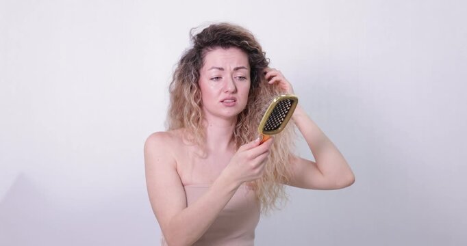 Unhappy woman trying to brush her tangled hair on light grey background