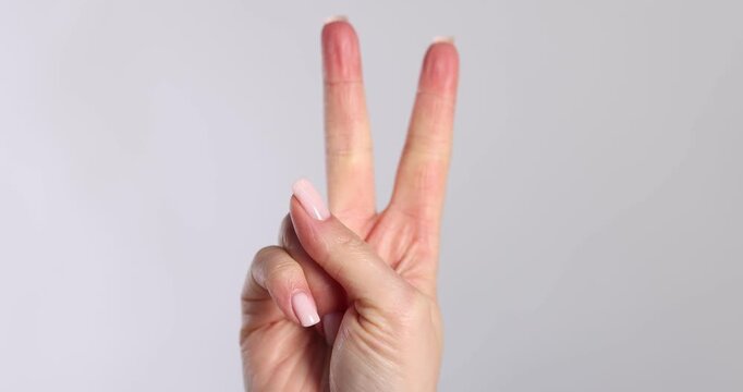 Woman showing V sign on light grey background, closeup