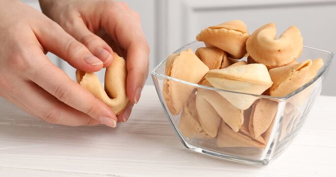 Woman breaking yummy fortune cookie with prediction at white wooden table, closeup