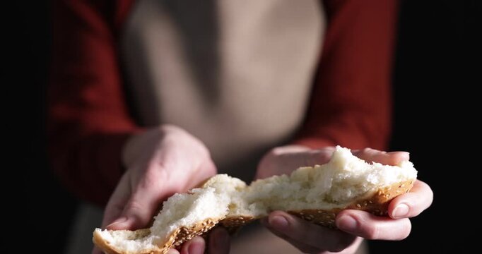 Woman breaking tasty bun with sesame seeds on black background, closeup