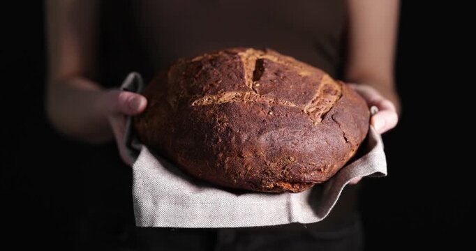 Woman holding loaf of rye bread on black background, closeup