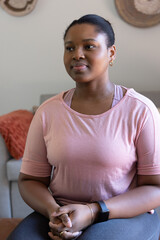 African American woman sitting on couch in living room wearing pink top and fitness smartwatch