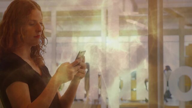 Seated woman tapping phone screen and reading creating golden wisps drifting over glass in business