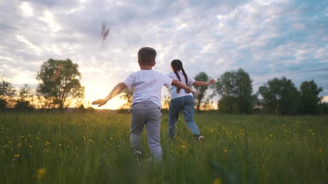 Two children running through field. Children running in a grass field. A young girl playing with her friends at a beautiful sunset outside. Two kids sprinting across a meadow lifestyle.