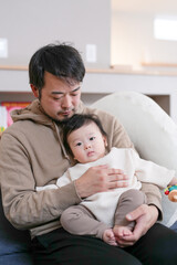 Obraz premium Soft lighting highlights tender father holding baby. Father gazes down with gentle affection. Baby rests peacefully in his arms. Warm tones suggest cozy, intimate moment. Ideal for family, parenting