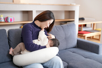 Obraz premium Mother cradles baby during breastfeeding session. Soft lighting highlights gentle moment. Comfortable couch provides calm, cozy setting. Mother smiles with tenderness and peace