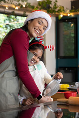 Asian mother and child baking in home kitchen, wearing Santa hat and holding metal sieve