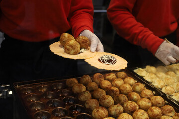 Fresh takoyaki balls being cooked on a hot iron pan at a Japanese market.