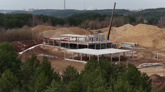 Ground-level view of a construction site with precast concrete beams, machinery, and building structure under development, highlighting industrial workflow and infrastructure progress.