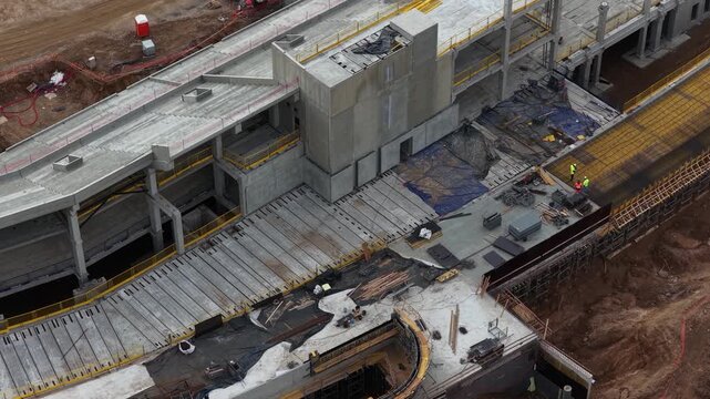 Drone shot of a large construction site with multi-level concrete structure, workers, scaffolding, and materials, highlighting infrastructure development and engineering progress.