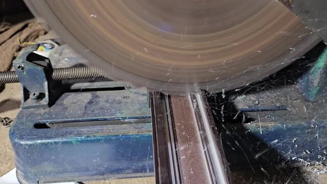 Close-up of a circular saw blade cutting through metal in an industrial workshop. The scene captures precision machining, sharp rotating blade, and manufacturing process.