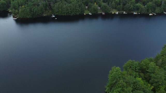 Aerial over the expansive wilderness of crown land located in the Tory Hill area of Highlands East, in southern Ontario, Canada. Flying above a still Buckskin Lake, with lakeside cottages.