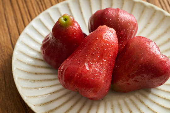 Four Red Wax Apples on a Vintage Fluted Ceramic Plate over a Natural Wood Grain Table