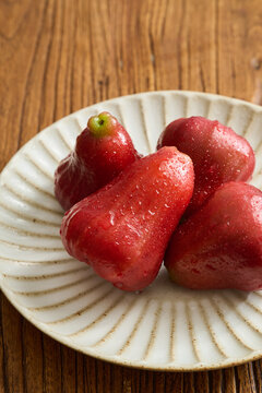 Four Red Wax Apples on a Vintage Fluted Ceramic Plate over a Natural Wood Grain Table