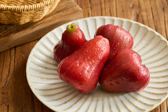 Four Red Wax Apples on a Vintage Fluted Ceramic Plate over a Natural Wood Grain Table
