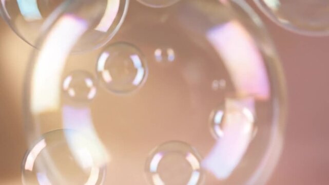 Close-up shot of several translucent soap bubbles floating in the air, reflecting light and creating iridescent colors against a soft, blurred background with a warm, inviting tone.