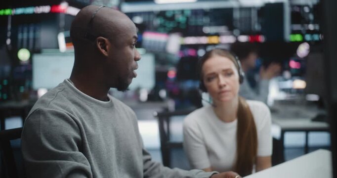 Senior Black Male Trader Explaining Market Volatility to Female Colleague. In Intensity Modern Trading Room, Experienced Man in Headset Guides Female Colleague Through Complex Real Time Analytics.