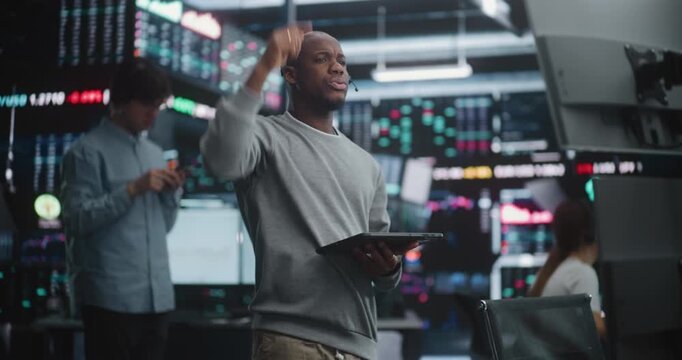 Diverse Stock Brokers Using Hand Signals and Gestures in Trading Pit Execute Instant Buy and Sell Orders. African American Trader in Headset Stands, Raising Hand Signal Trade, Holding Digital Tablet.
