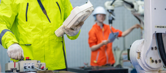 Male Engineer Operating a Robot Arm with a Handheld Controller Automation Engineer Using Teach Pendant for Precision Control Engineer in Safety Gear Checking Robot System Operation. © BESTIMAGE