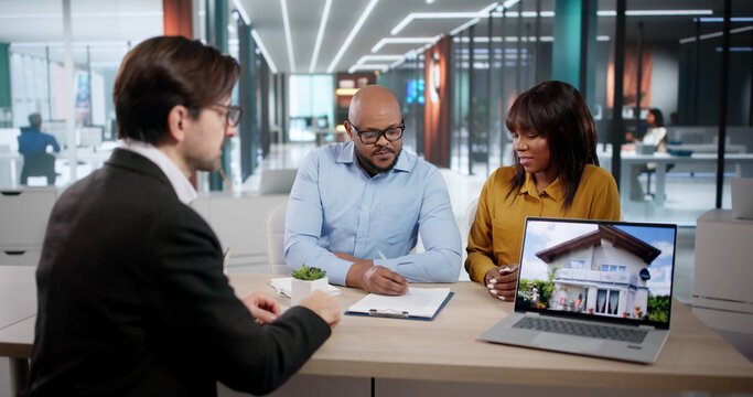 Happy Couple And Their Real Estate Agent Reviewing Contracts During Family