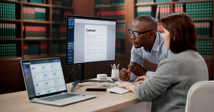 Two Lawyers And A Paralegal Reviewing Contracts Carefully On Laptop Together