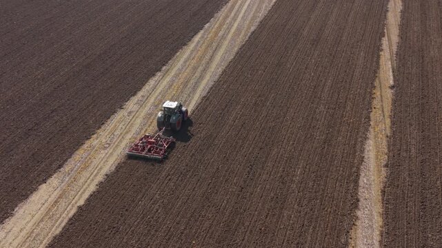 Aerial drone view of a tractor harrowing farmland in northern Italy, preparing soil for crops in a productive agricultural landscape.