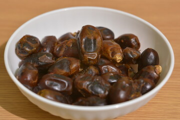 Fototapeta premium Hand picking dried dates from white bowl on wooden table