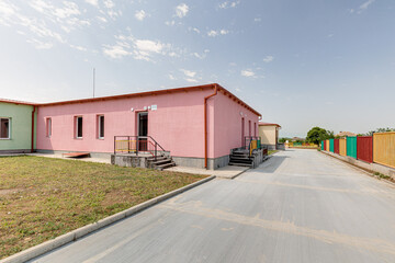 Fototapeta premium Outdoor view of a contemporary educational facility featuring bright colored railings, pink and beige buildings, concrete entrance stairs and a paved walkway under a clear sky.